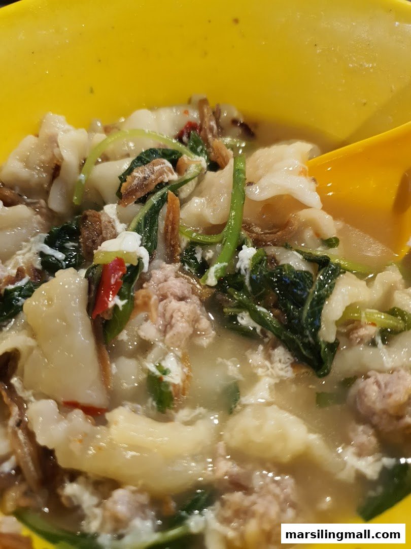 A close-up of a hearty bowl of handmade noodle soup with minced meat, vegetables, and anchovies.