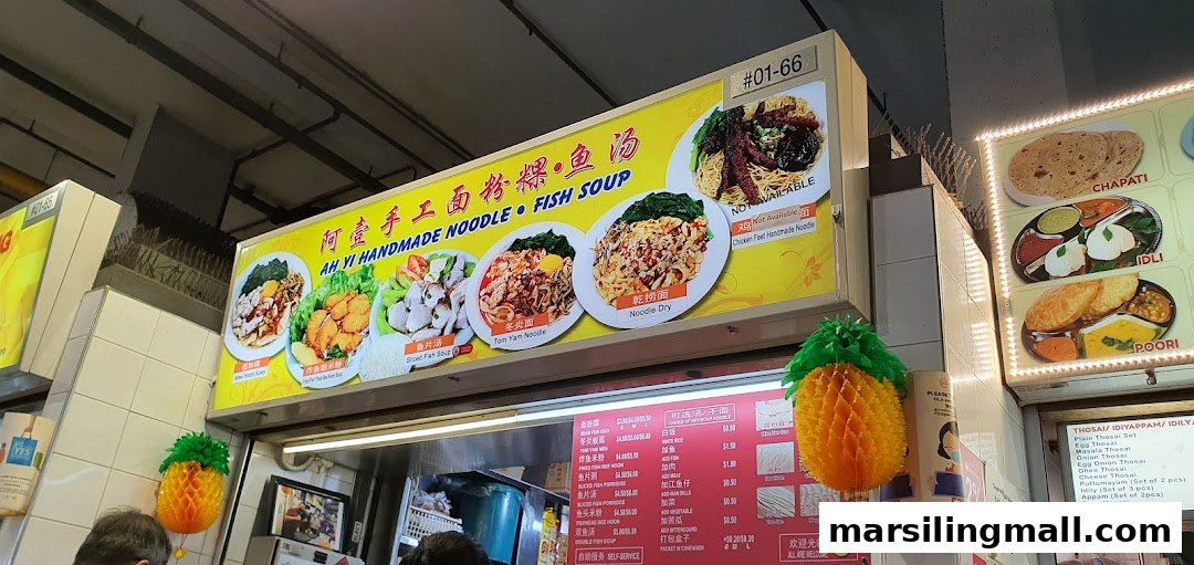 A bright signboard displaying various noodle and fish soup dishes with a detailed menu board below.