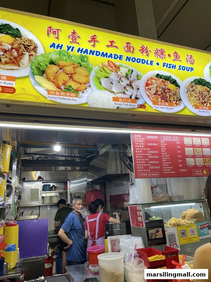 A bustling counter at Ah Yi Handmade Noodle Fish Soup, showcasing staff, kitchen operations, and a vibrant menu signboard.