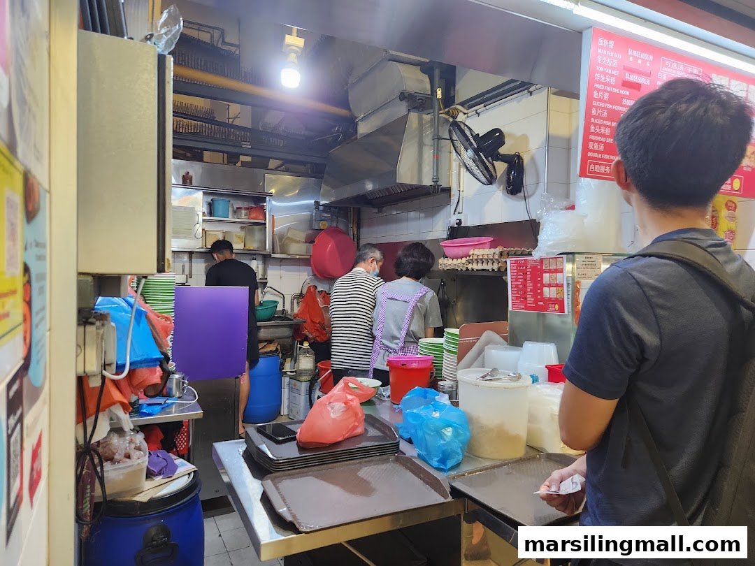 A customer views the menu board at Ah Yi Handmade Noodle Fish Soup, showing various noodle and soup dishes.