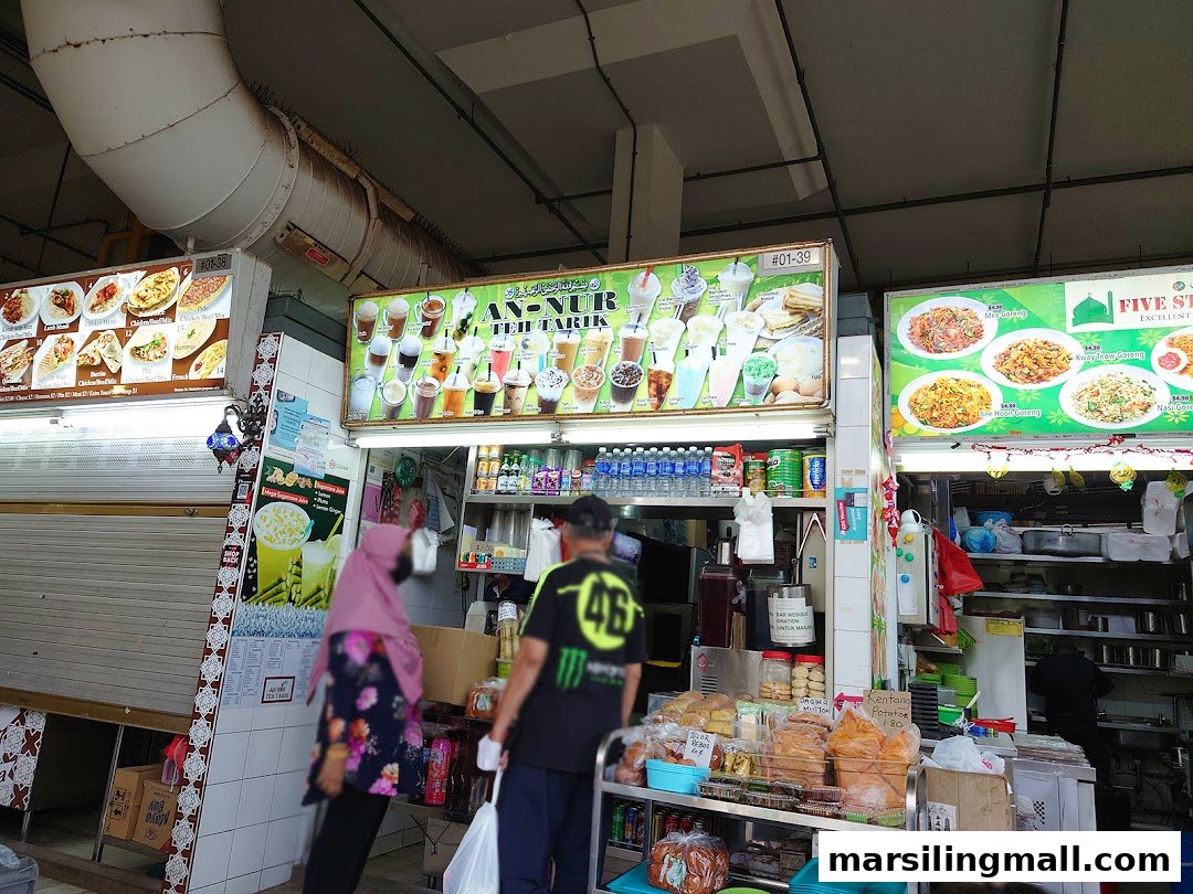 Vibrant shop front of An-Nur Teh Tarik stall, showcasing diverse drinks and food options with customers.