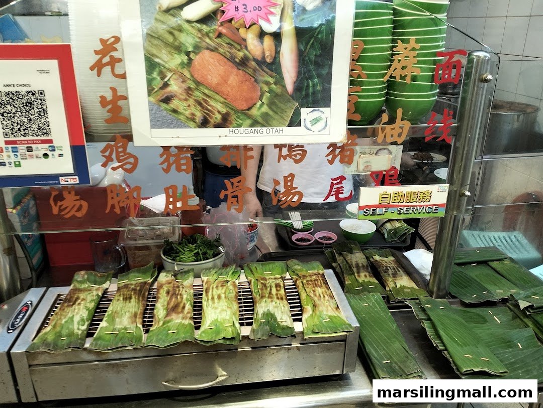 A food stall counter at AnnS Choice featuring grilled otah wrapped in banana leaves and a self-service setup.