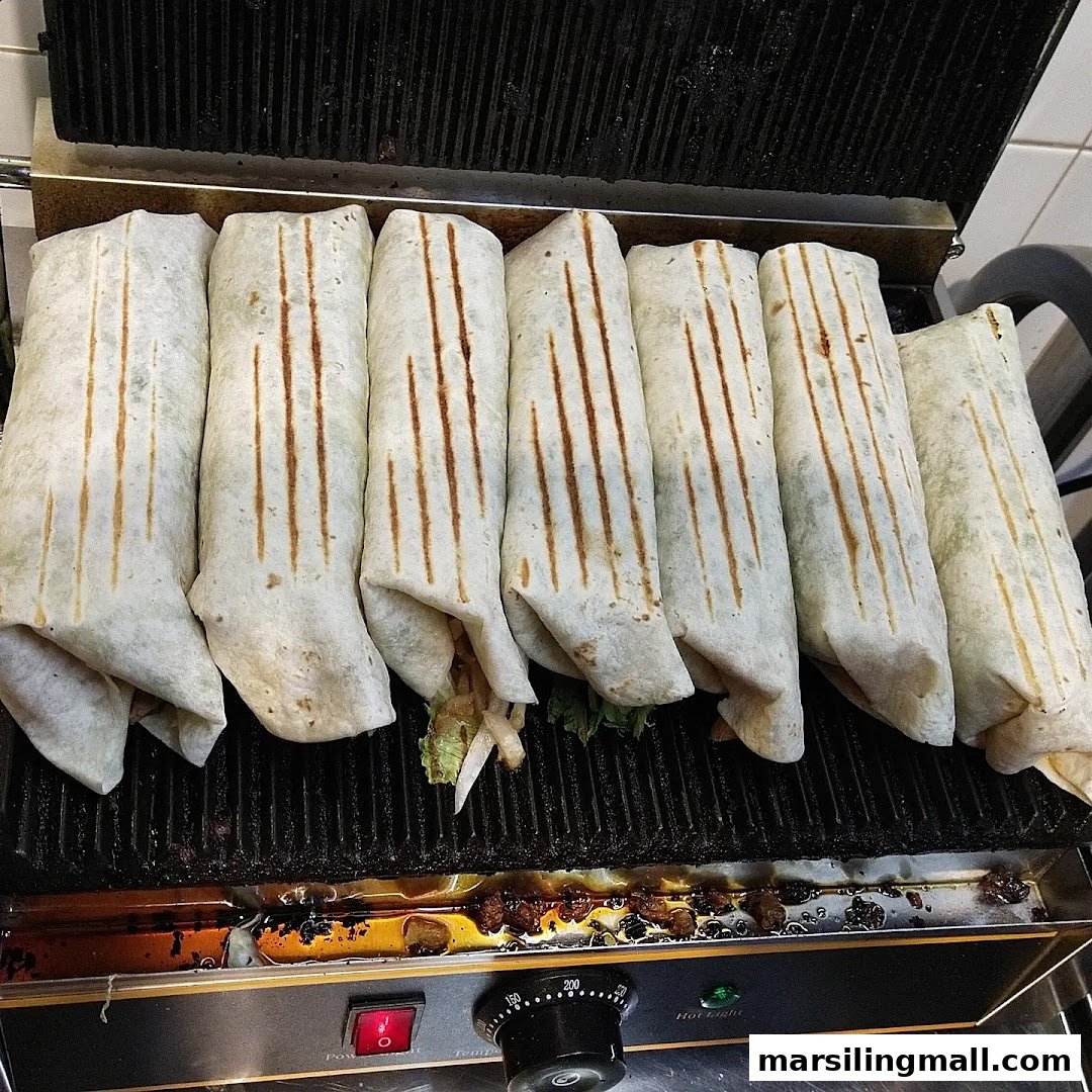 Several freshly grilled wraps or kebabs cooking on a commercial panini press.