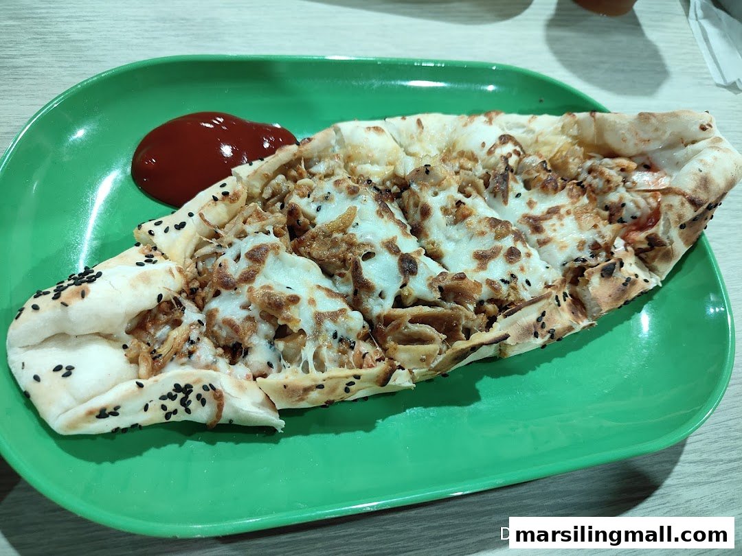A boat-shaped flatbread topped with melted cheese, meat, and black sesame seeds, served with red sauce.