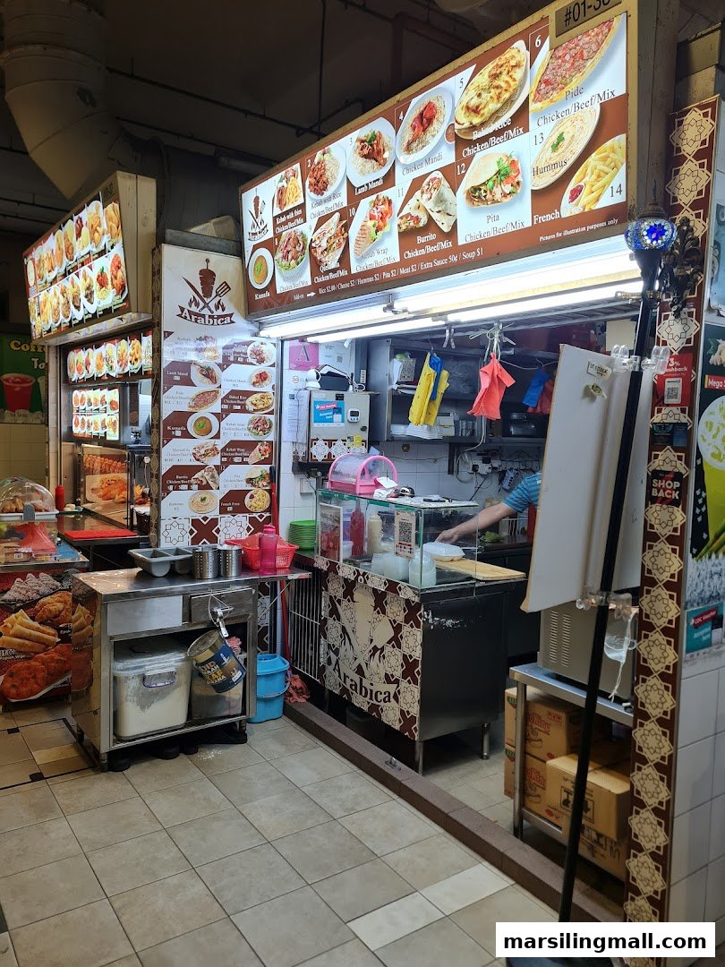 A vibrant food stall named Arabica Kebab, featuring a large illuminated menu board and a staff member.