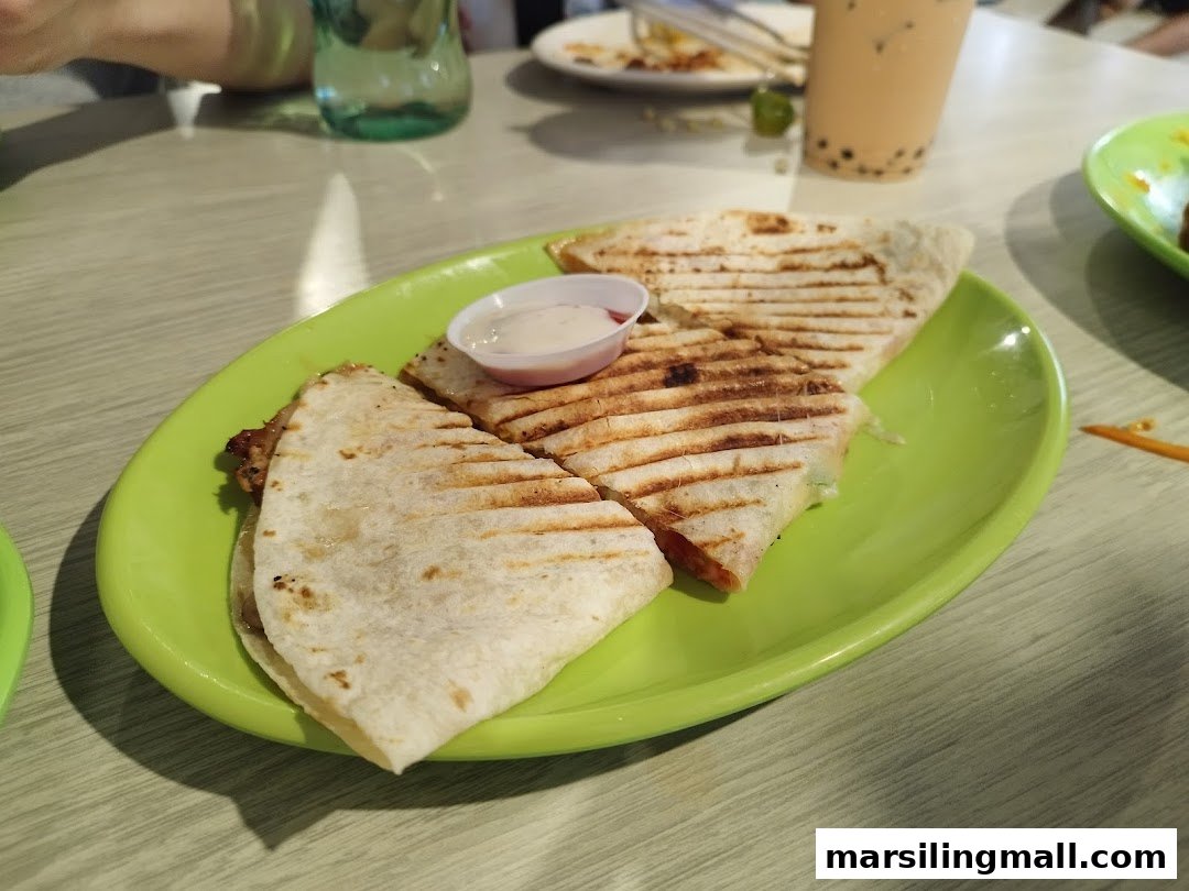 A vibrant green plate holds grilled quesadillas with a side of dipping sauce on a light-colored table.