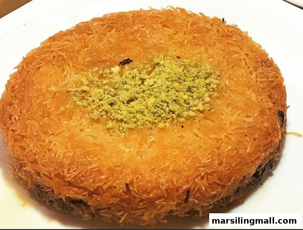 A delicious, golden-brown Kunafa dessert topped with vibrant green ground pistachios on a white plate.
