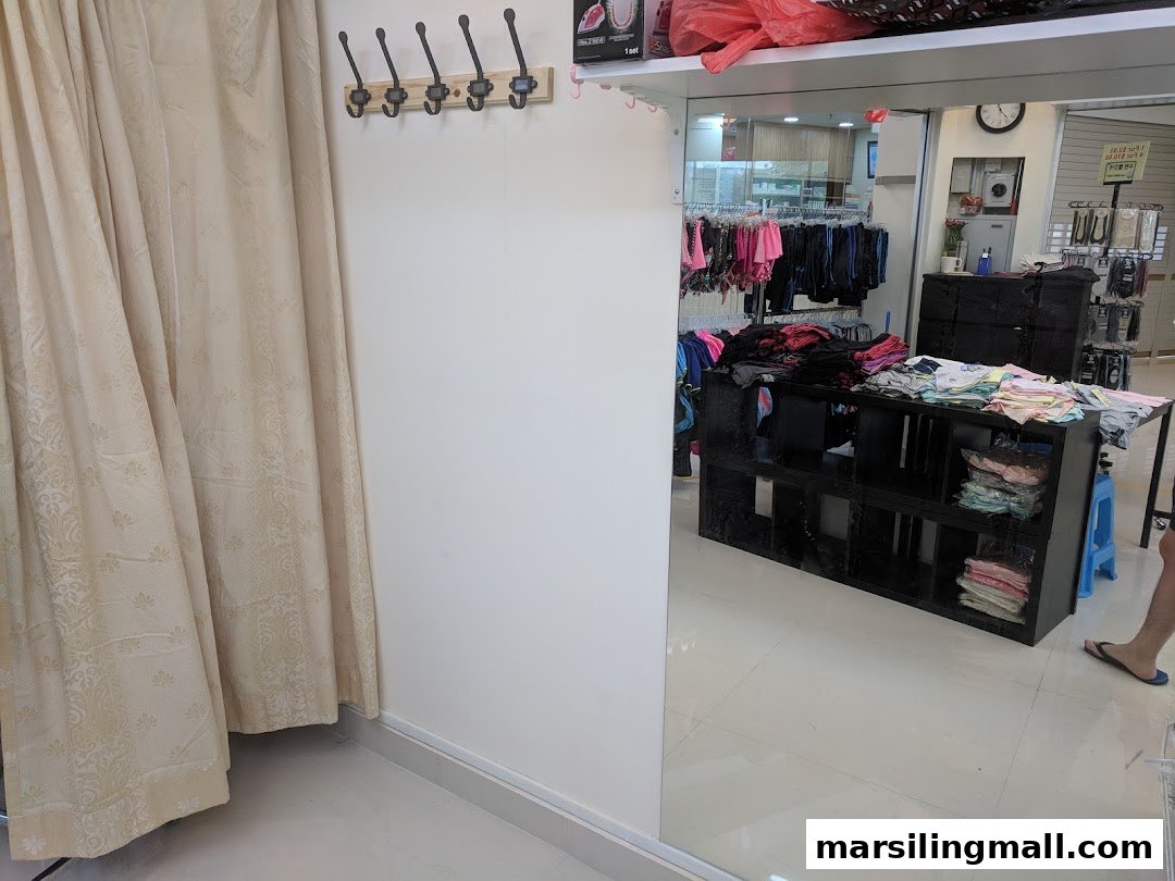 Interior view of a clothing alteration shop, featuring a changing room, coat hooks, and a large mirror reflecting clothing displays.