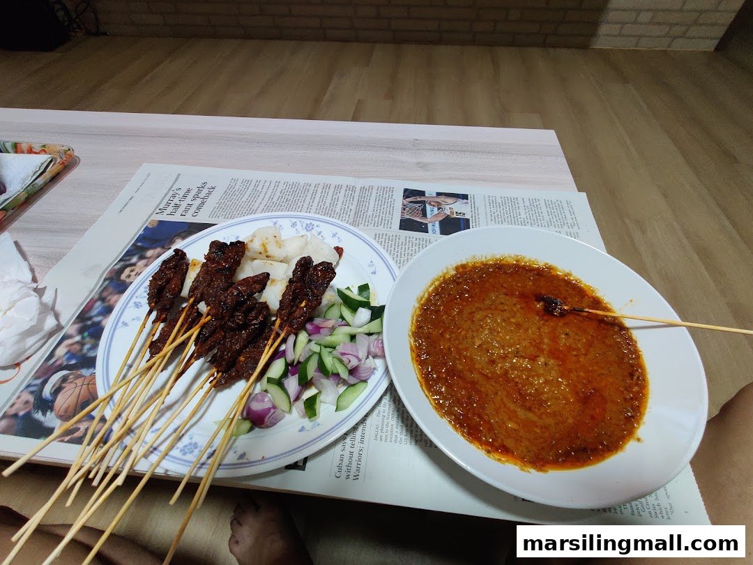 A plate of grilled satay skewers with peanut sauce, rice cakes, cucumber, and onions.