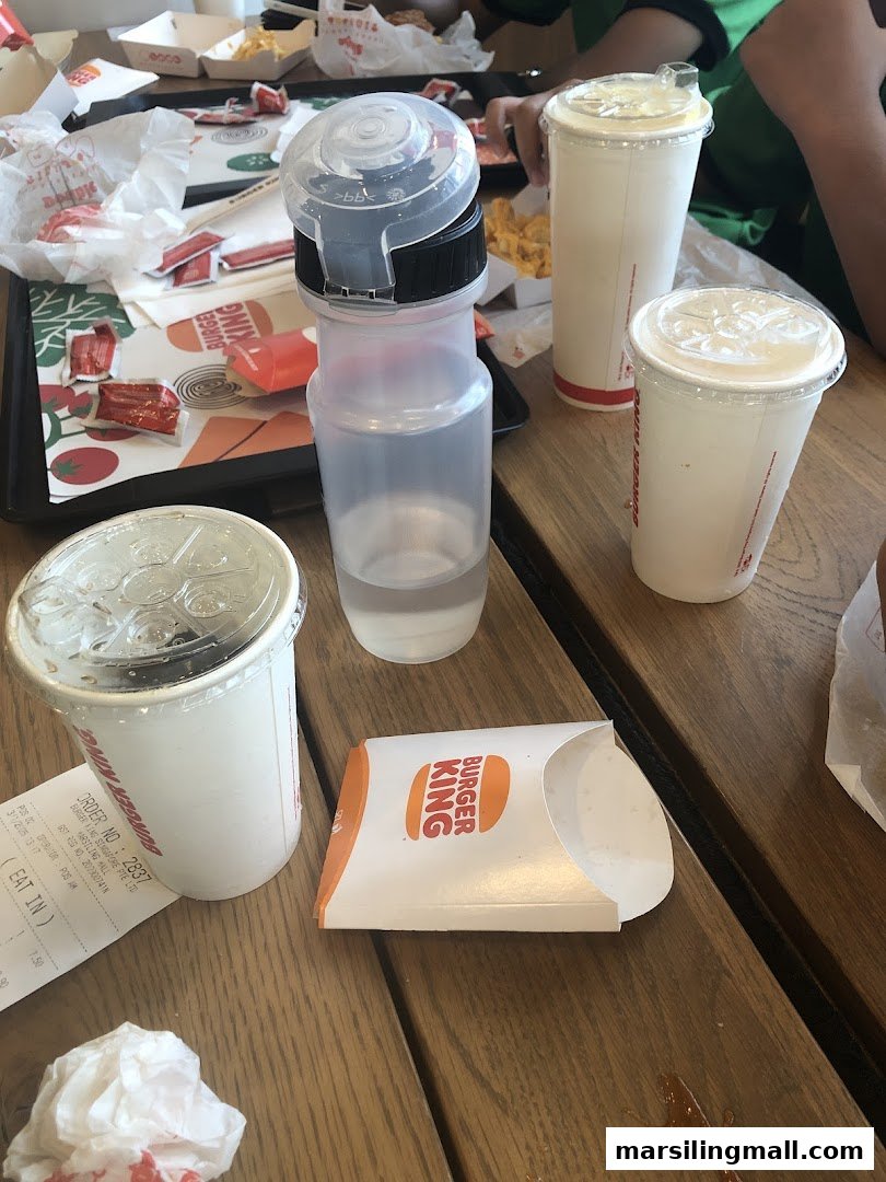 A wooden table at Burger King with empty food packaging, drinks, and a receipt.