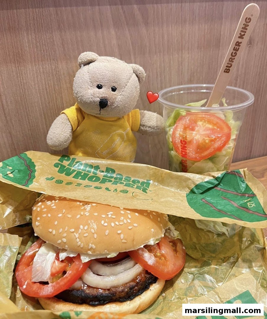 A Burger King Plant-Based Whopper, a side salad, and a cute teddy bear on a wooden surface.