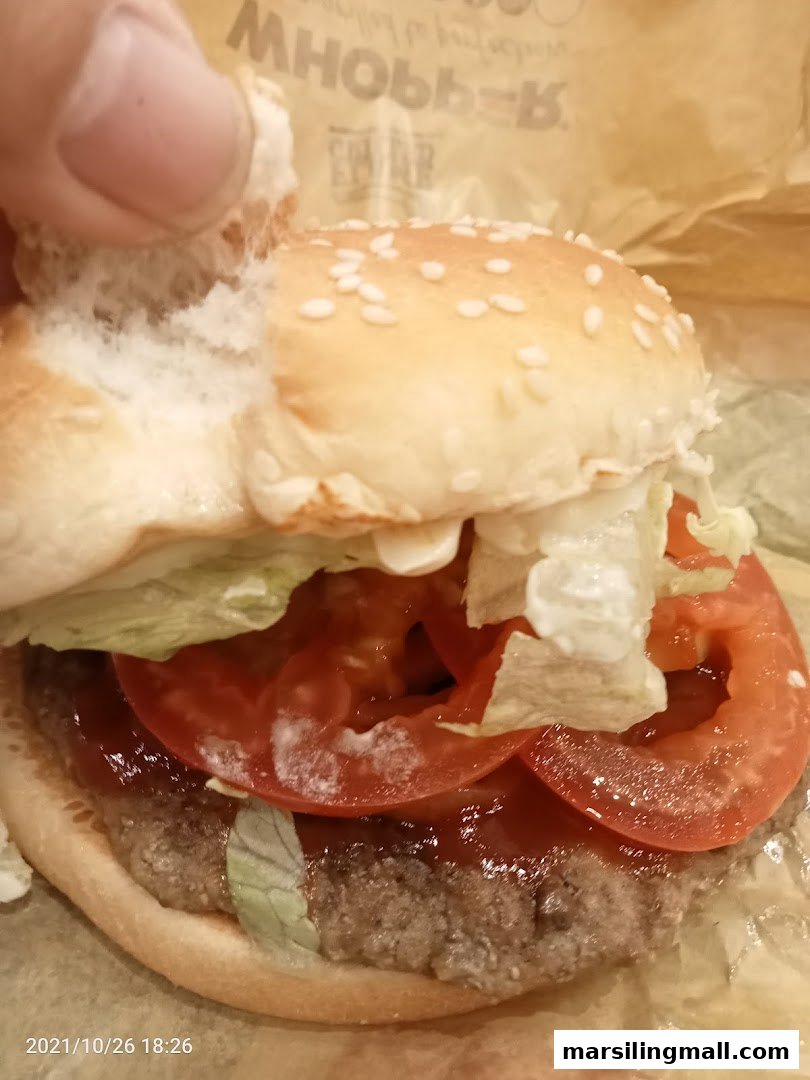 A close-up of a Burger King burger with a sesame seed bun, patty, lettuce, and tomato.