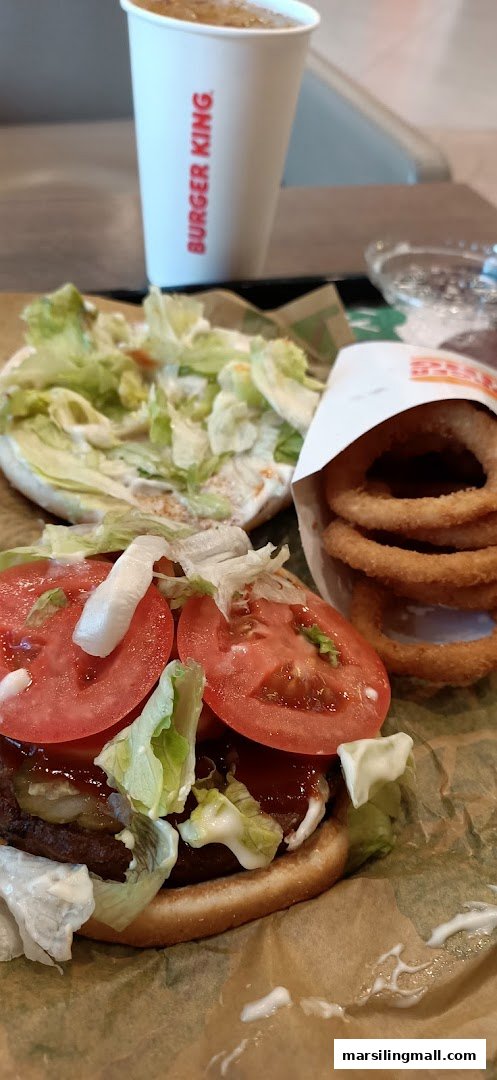 A deconstructed Burger King burger with fresh toppings, onion rings, and a drink.