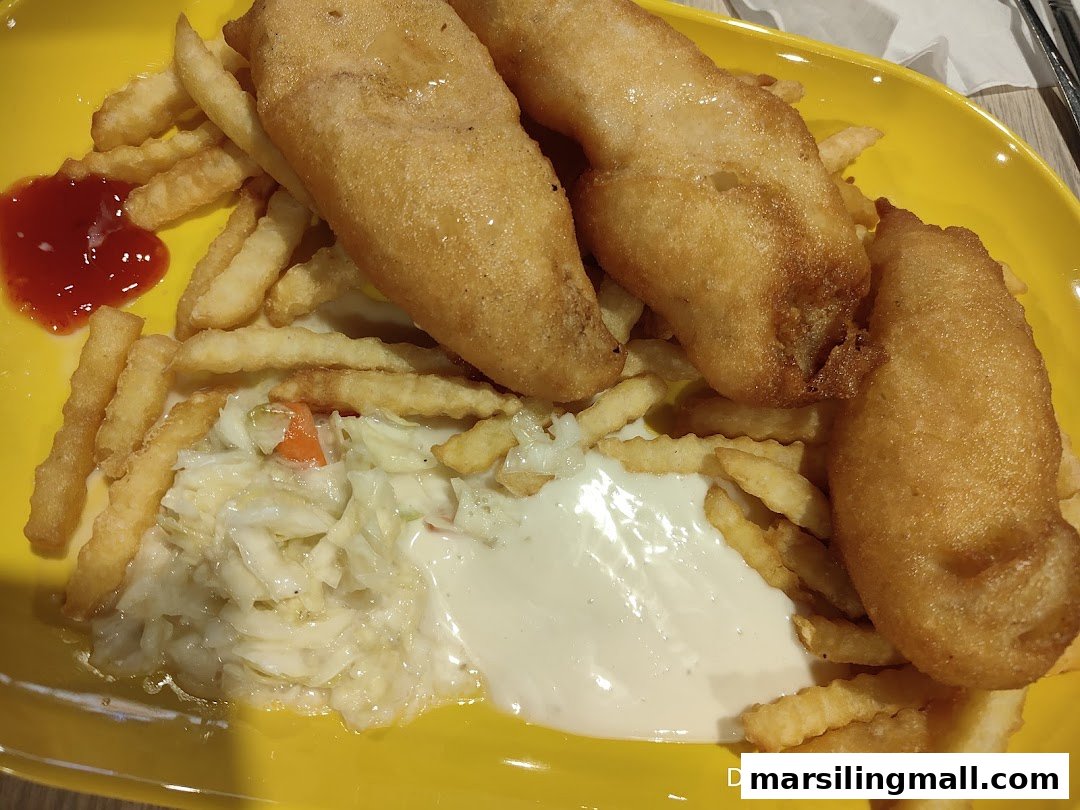 A vibrant yellow plate holds golden-fried fish, crispy fries, creamy coleslaw, and sauces.