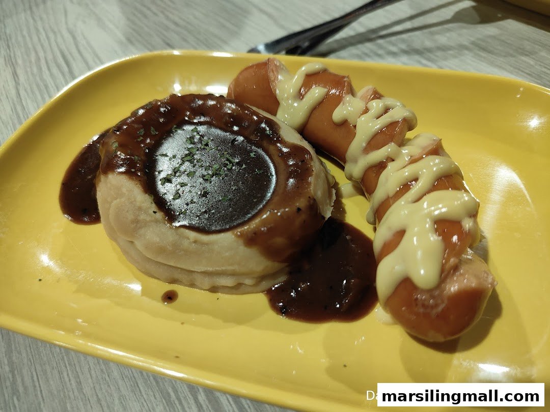 A vibrant yellow plate holds a dish of mashed potatoes with gravy and a sausage drizzled with mustard.