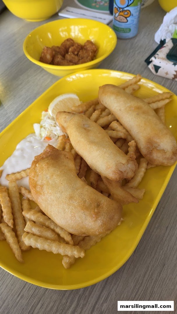 A vibrant yellow plate holds golden-fried fish and crispy fries, served with coleslaw and tartar sauce.