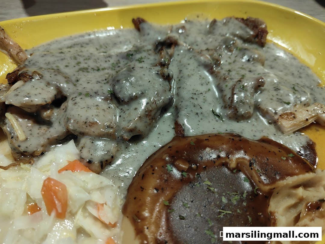 A close-up of a dish featuring grilled meat with creamy sauce, mashed potatoes, and coleslaw on a yellow plate.