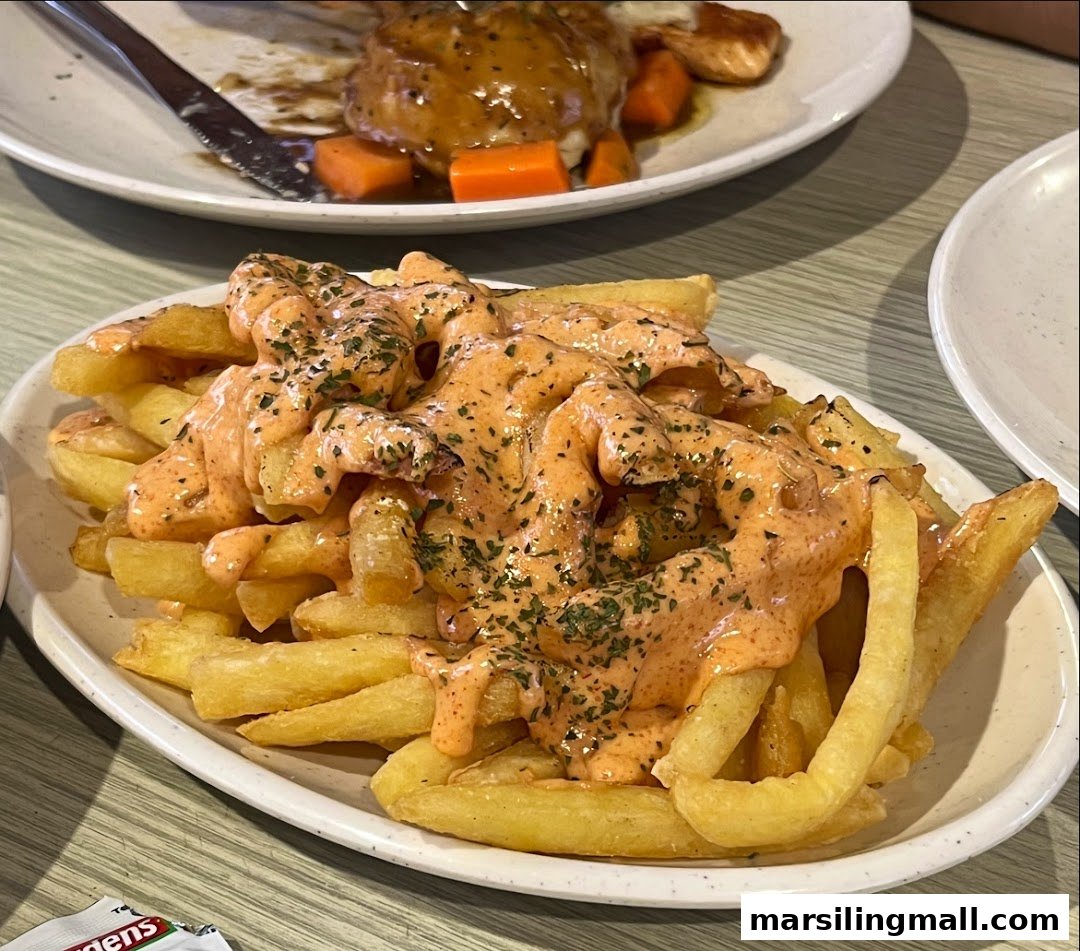 A plate of golden fries generously topped with creamy sauce and herbs, with another dish in the background.