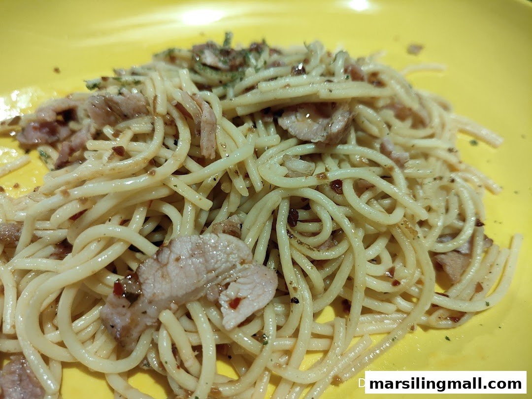 A close-up of spaghetti with sliced meat and herbs on a vibrant yellow plate.