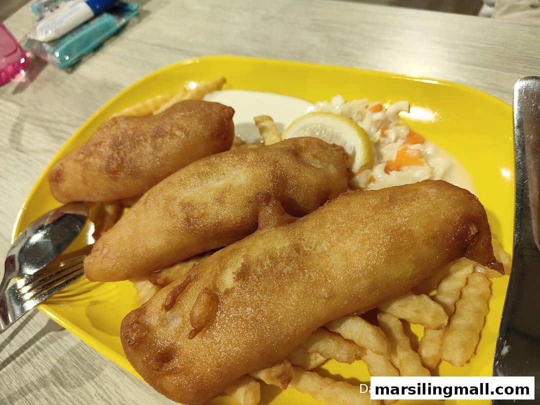A vibrant yellow plate holds golden-brown fish and chips with coleslaw and lemon.