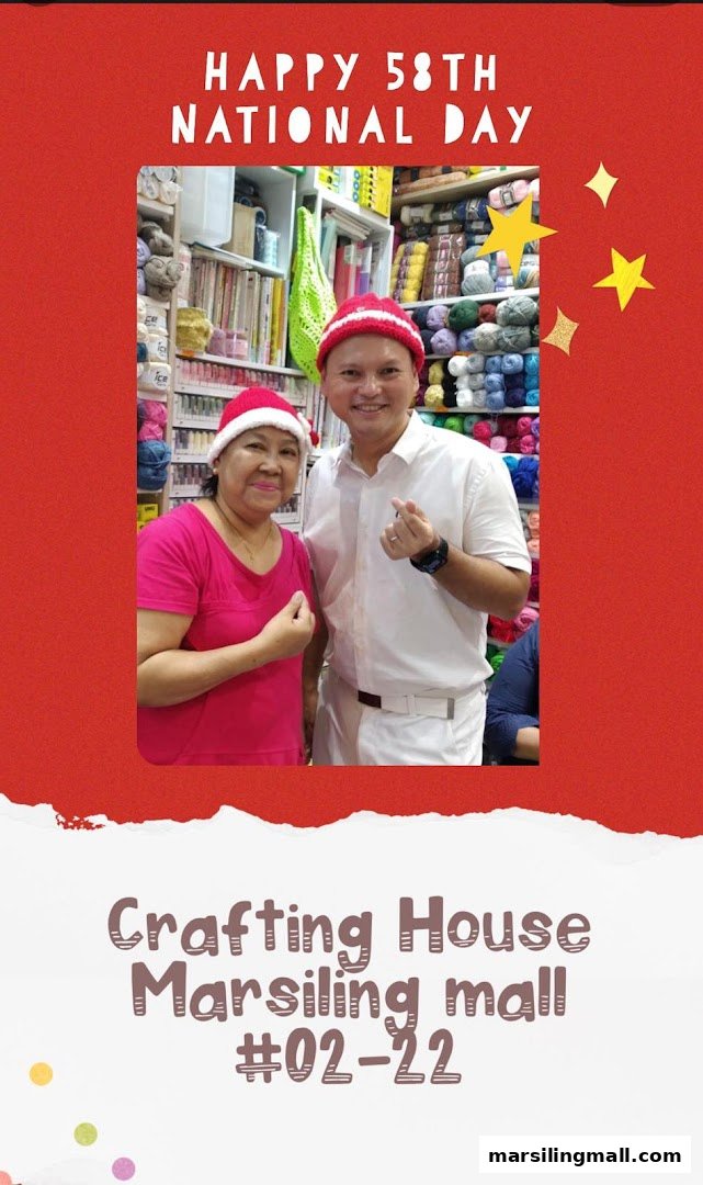 Two smiling individuals in Santa hats pose inside Crafting House, surrounded by colorful yarn and craft supplies.