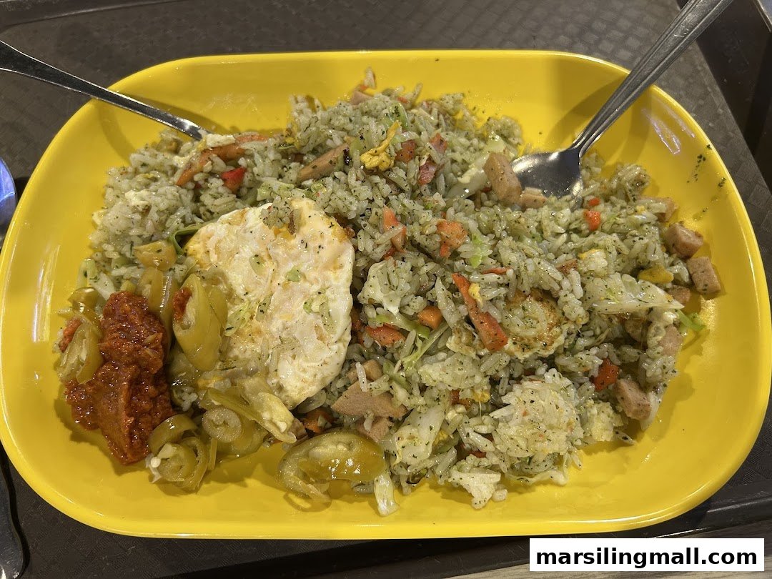 A vibrant yellow plate holds green fried rice with a fried egg, chili paste, and pickled peppers.