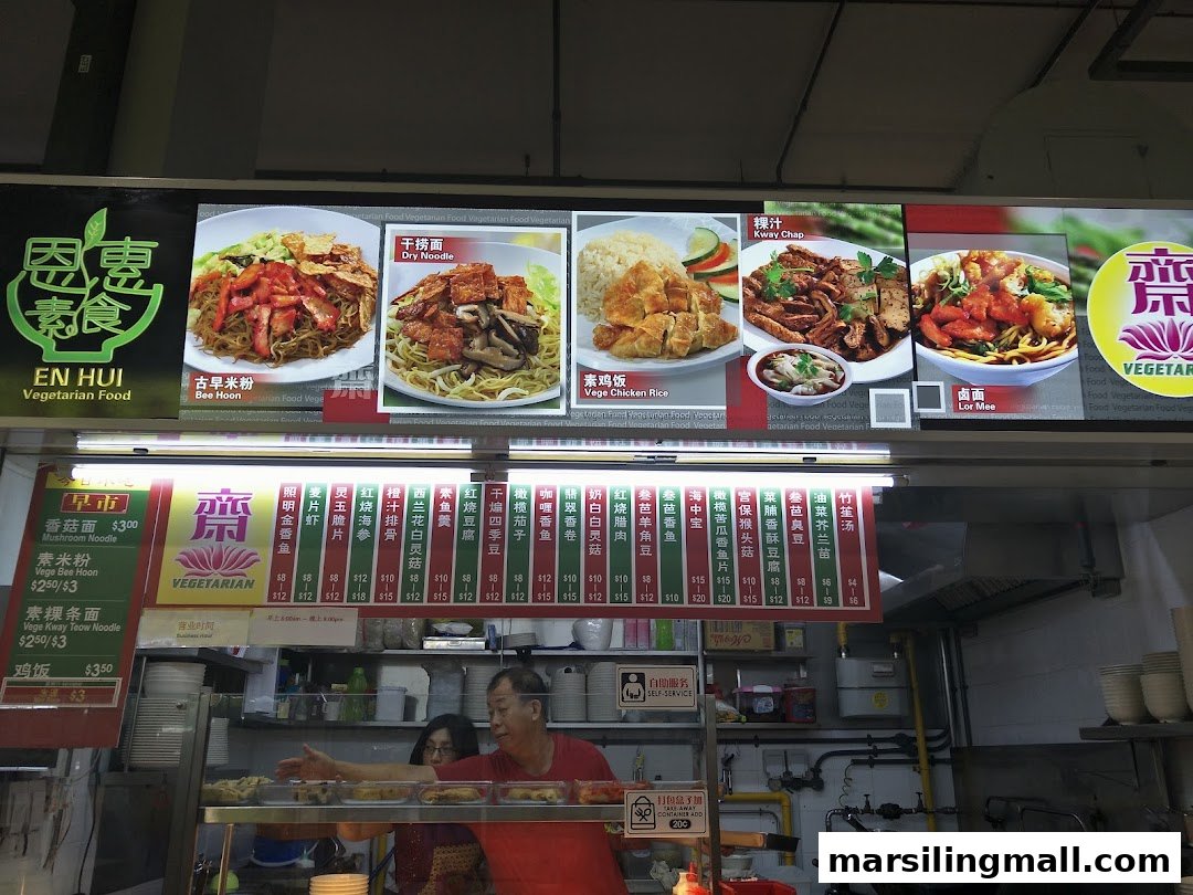 A vibrant vegetarian food stall displaying its diverse menu with images and prices, featuring staff serving customers.