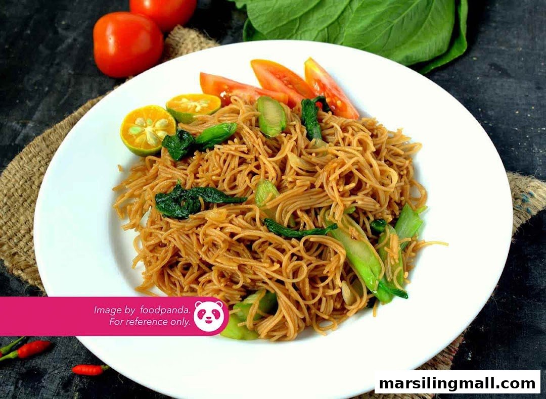 A plate of savory vegetarian stir-fried noodles with vegetables, lime, and tomato garnishes.