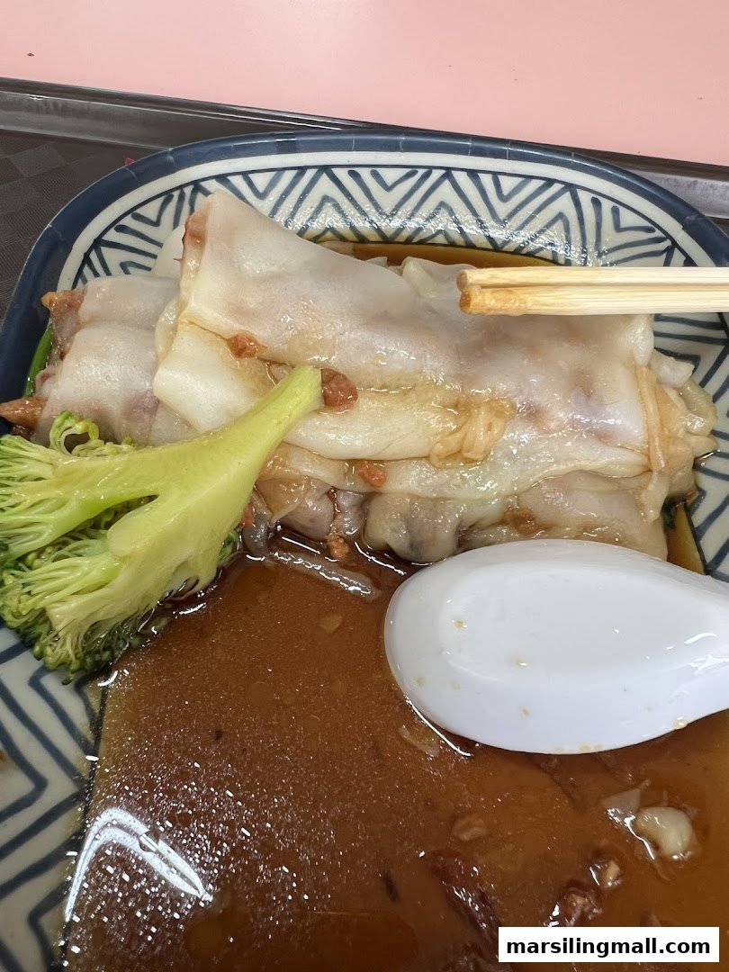 A close-up of Hong Kong style chee cheong fun with sauce, broccoli, and chopsticks in a patterned bowl.