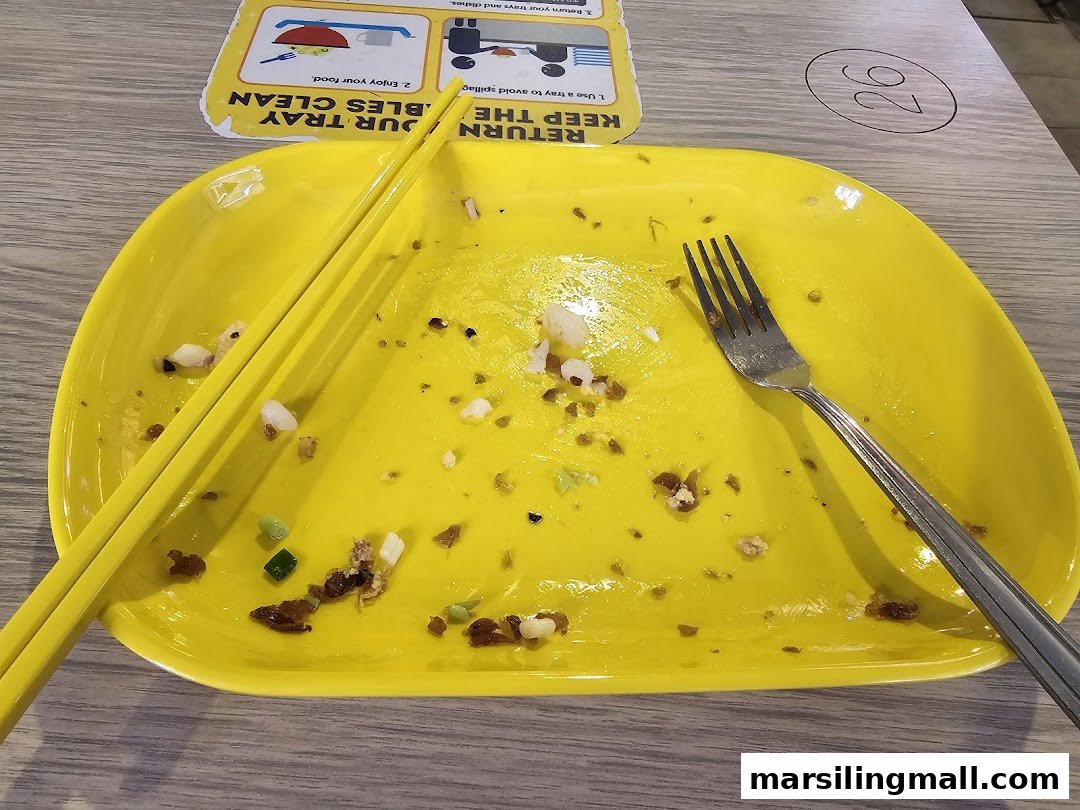 A bright yellow plate with leftover food, chopsticks, and a fork on a wooden table.