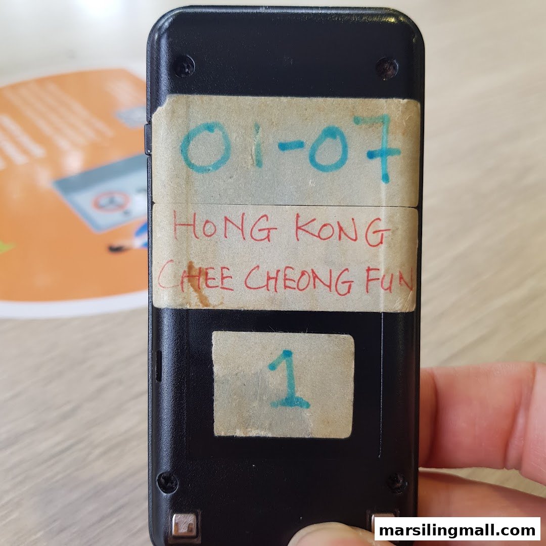 A close-up of a black pager with handwritten labels indicating 'Hong Kong Chee Cheong Fun' and a unit/order number.