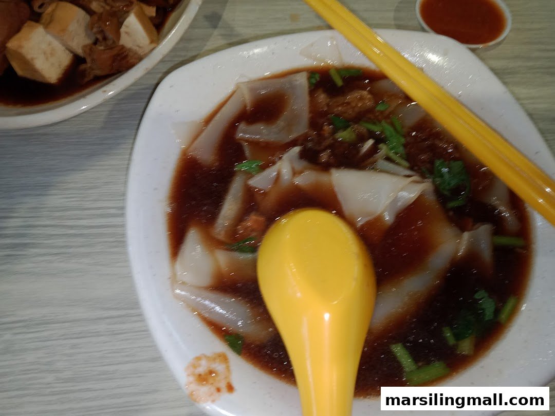 A close-up of a delicious bowl of kway chap with flat rice noodles and a side dish.
