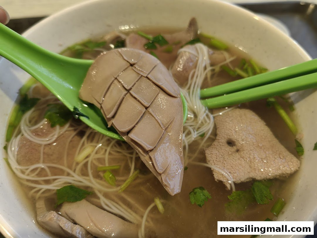 A close-up of a bowl of pig's organ soup with vermicelli noodles and various offal.