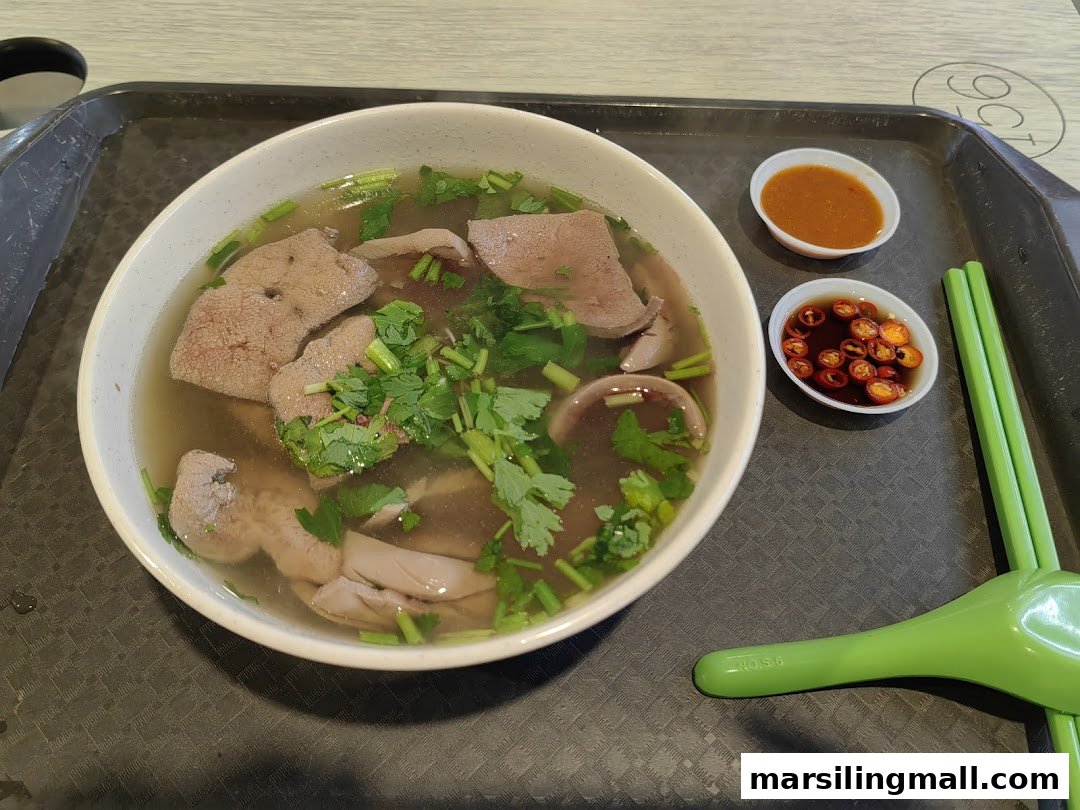 A steaming bowl of pig's organ soup with liver, intestines, and cilantro, served with chili sauces.