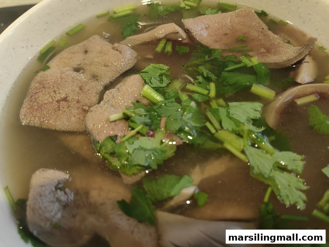 A close-up of a bowl of pig organ soup with liver, intestines, and fresh cilantro.
