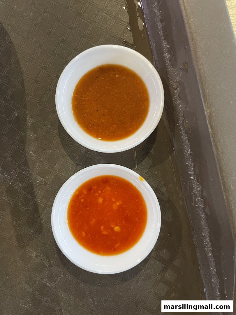 Two small white bowls of dipping sauces, one red chili and one brown savory, on a dark tray.