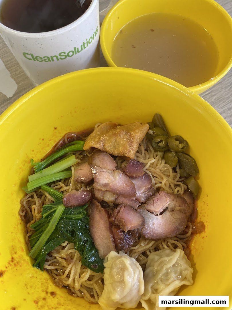 A vibrant bowl of wanton noodles with char siew, vegetables, and a side of soup and tea.