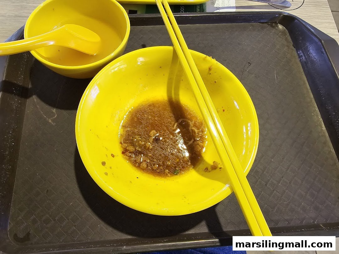 A yellow bowl with leftover noodles and chopsticks on a dark tray, indicating a finished meal.