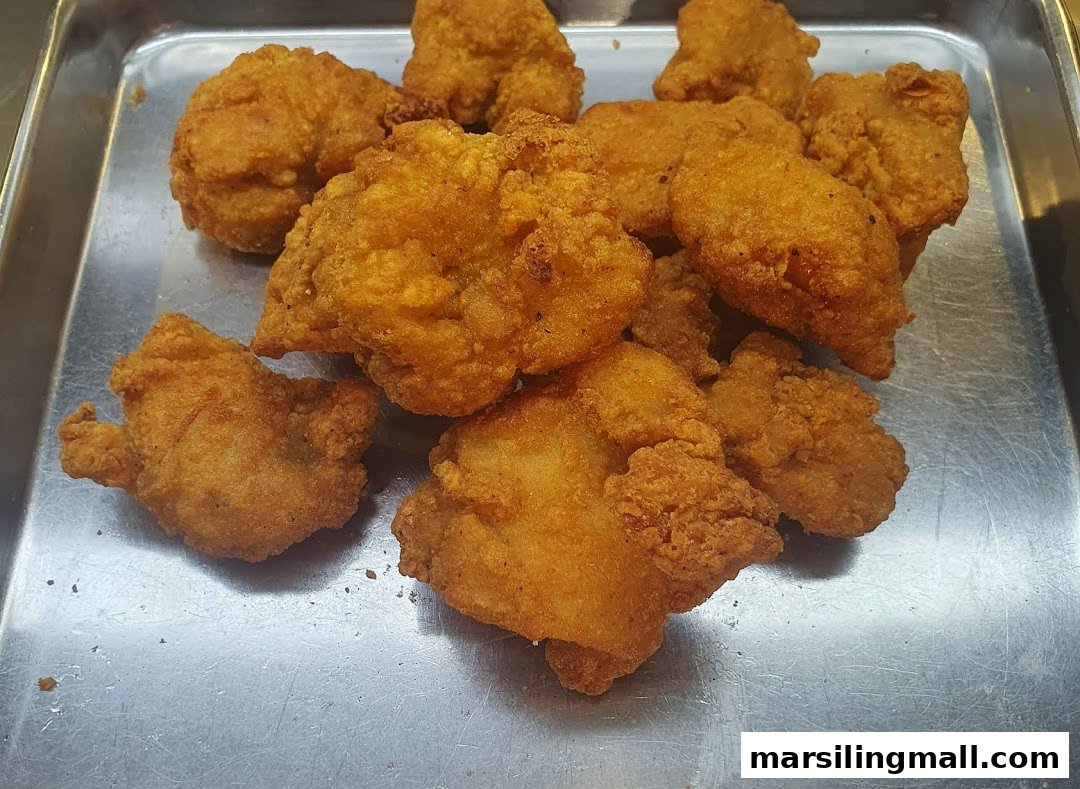 A close-up of golden-brown fried chicken pieces on a metal tray.