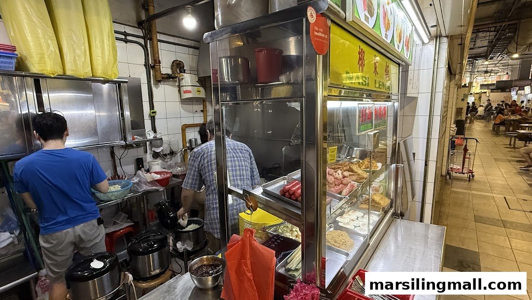A bustling food stall kitchen with staff preparing dishes and a display of fresh ingredients.