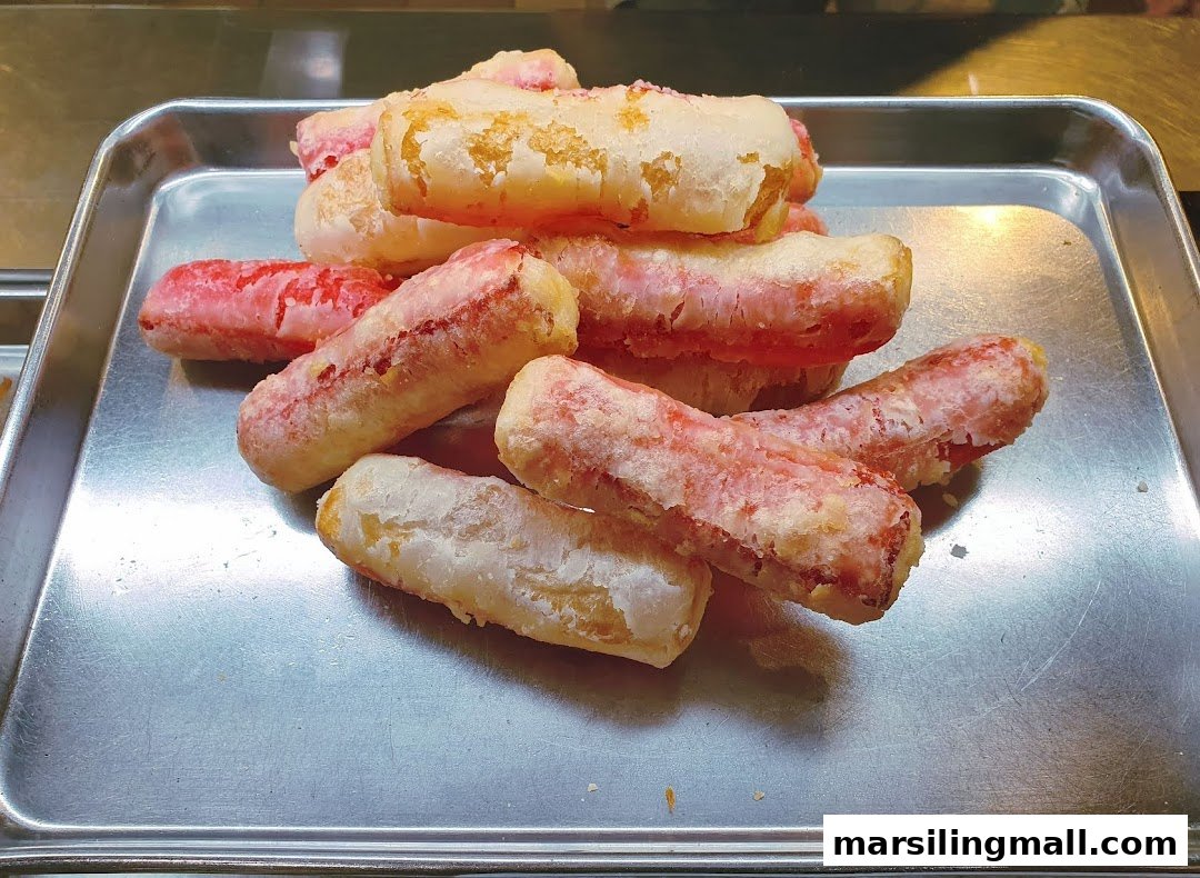 A close-up of several golden-fried dough sticks, some with a reddish tint, on a metal tray.