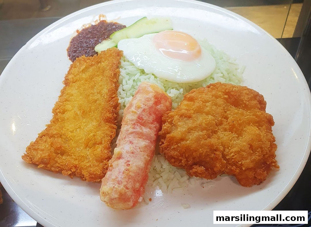 A plate of Nasi Lemak with green rice, fried fish, chicken, sausage, sambal, and a sunny-side-up egg.