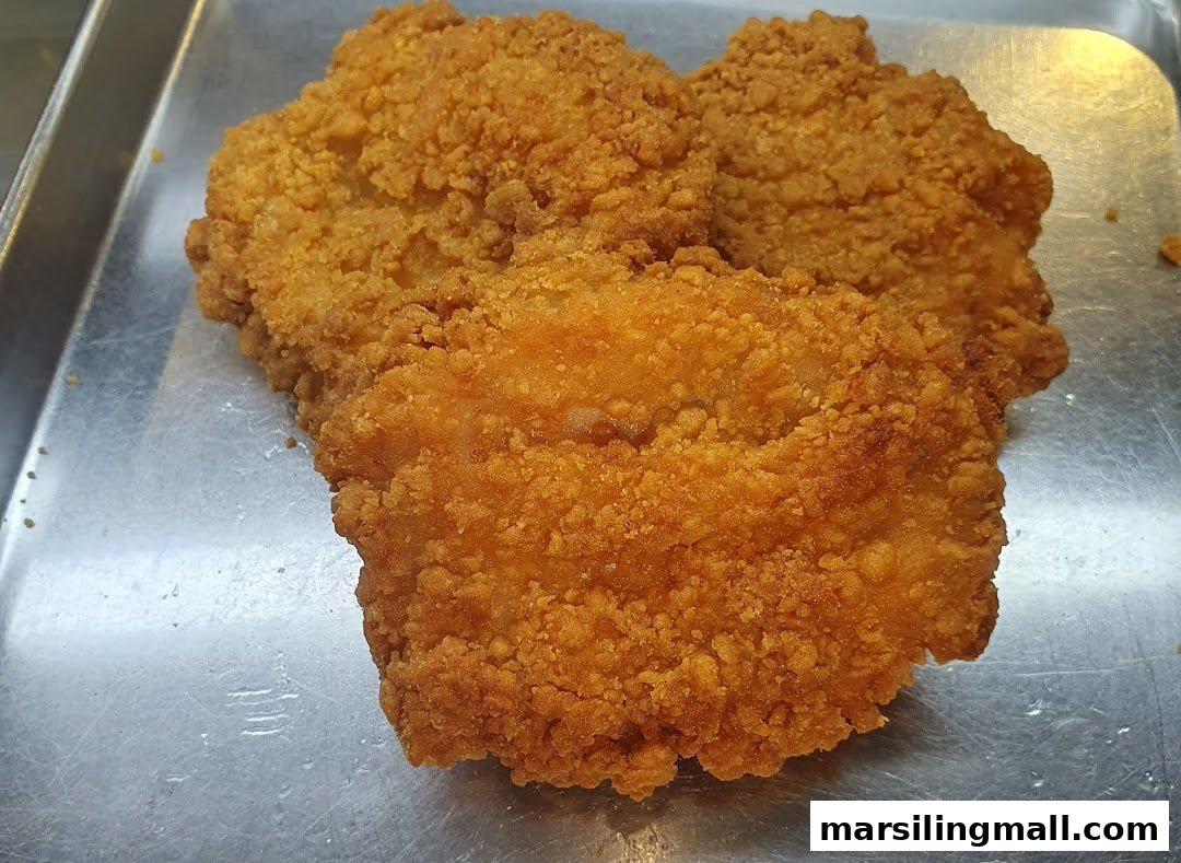 Close-up of several golden-brown, crispy fried chicken cutlets on a metal tray.
