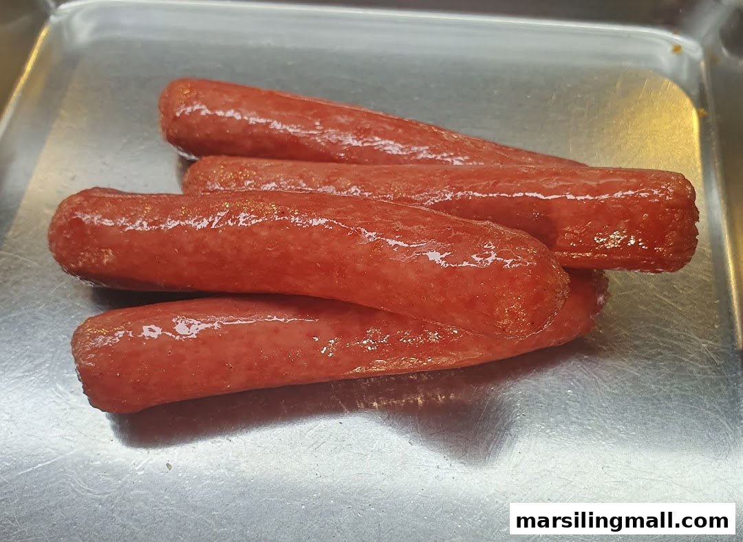 Four glossy, reddish-brown sausages are neatly arranged on a reflective metal tray.