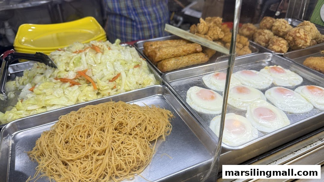 A display of various prepared food items including noodles, cabbage, fried eggs, and fried chicken.