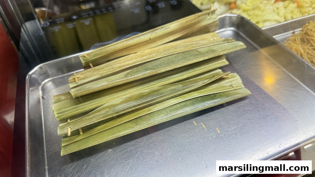 Several pieces of traditional Otak-Otak wrapped in palm leaves displayed on a metal tray.