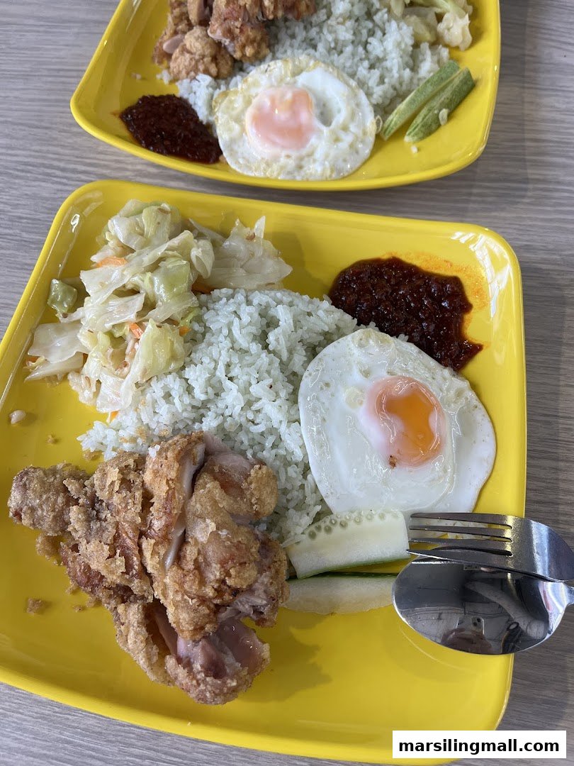 Two vibrant yellow plates of Nasi Lemak with crispy fried chicken, sunny-side-up eggs, and spicy sambal.