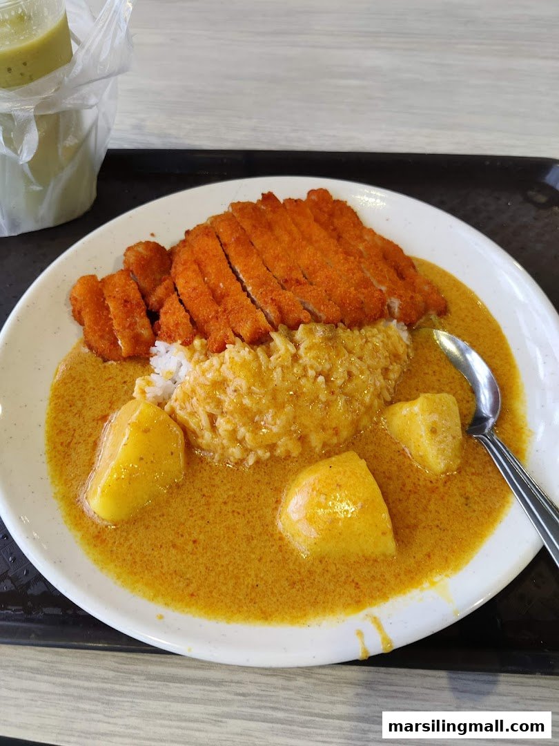 A plate of golden curry with crispy katsu, rice, and potatoes, served with a drink.