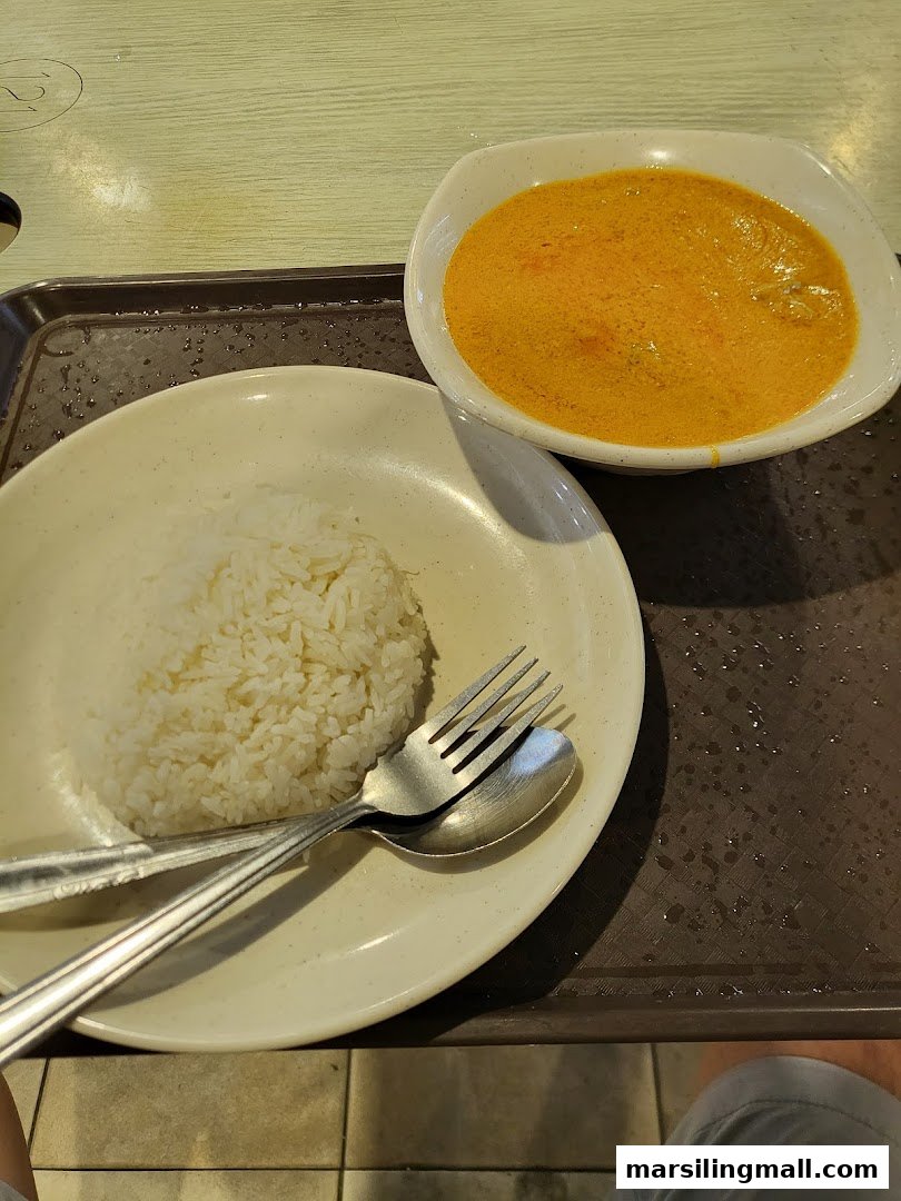 A bowl of rich orange curry and a plate of white rice on a brown tray.