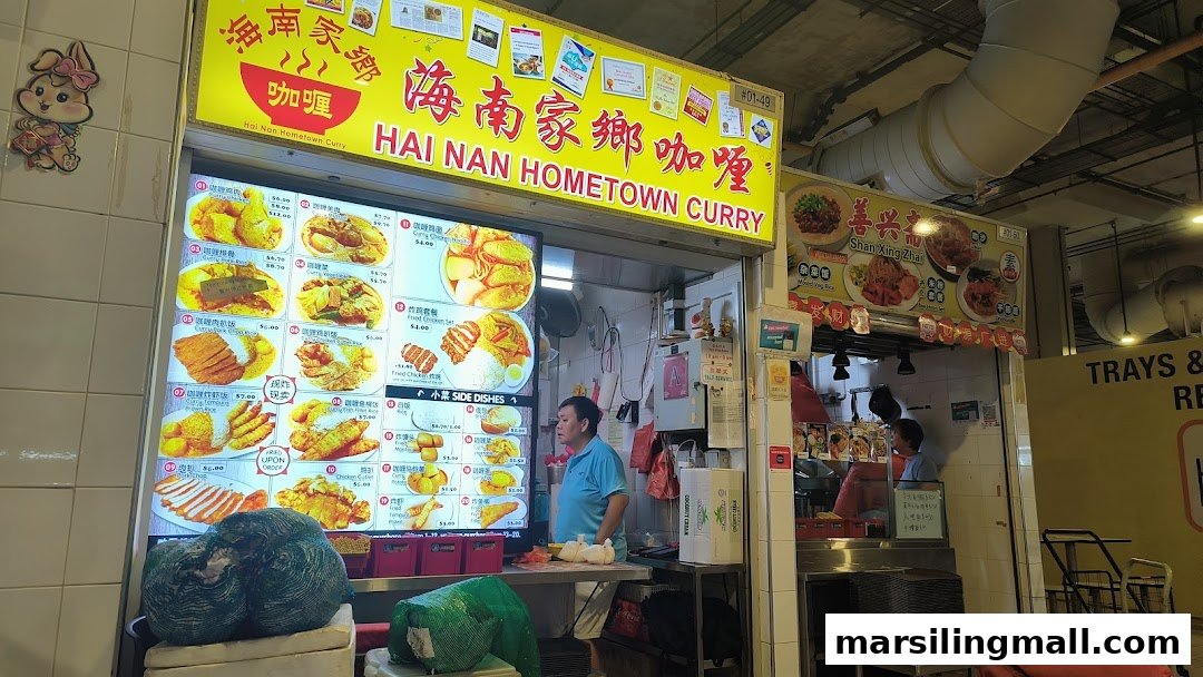 A vibrant view of Hai Nan Hometown Curry stall, featuring its digital menu board and a staff member.
